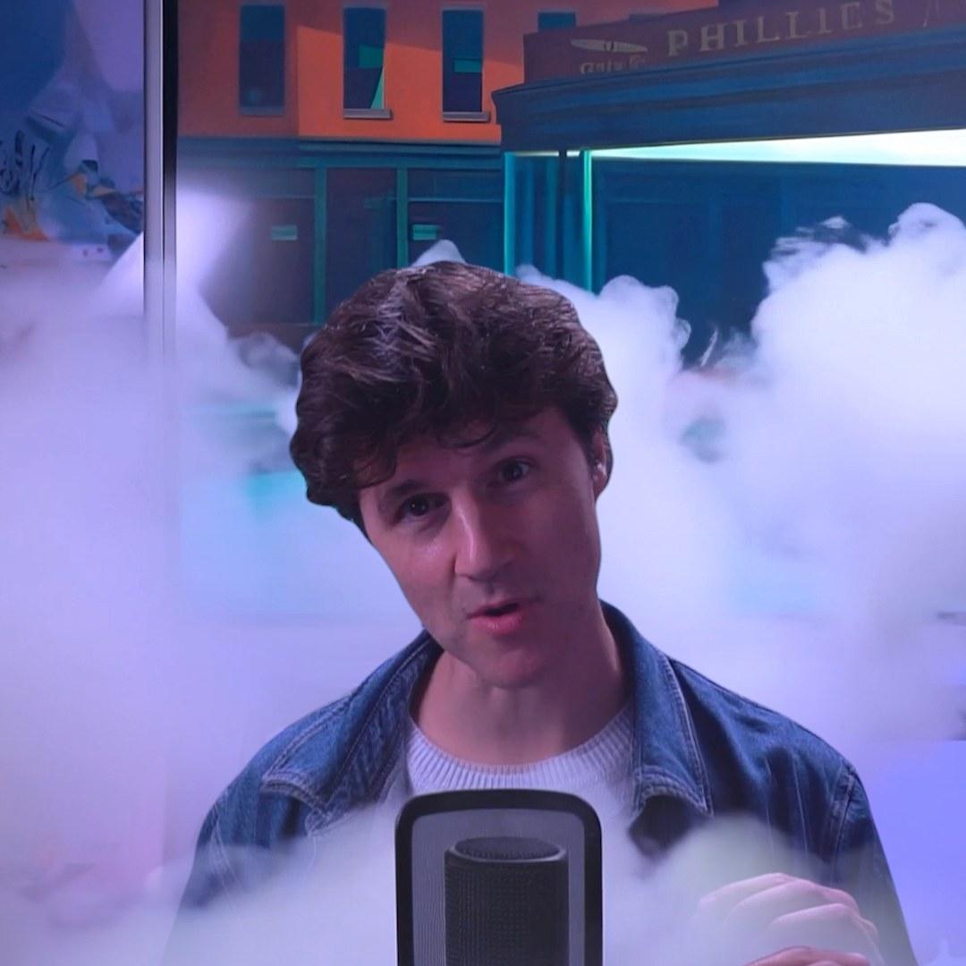 Danny at a microphone surrounded by fake smoke in front of a painted backdrop