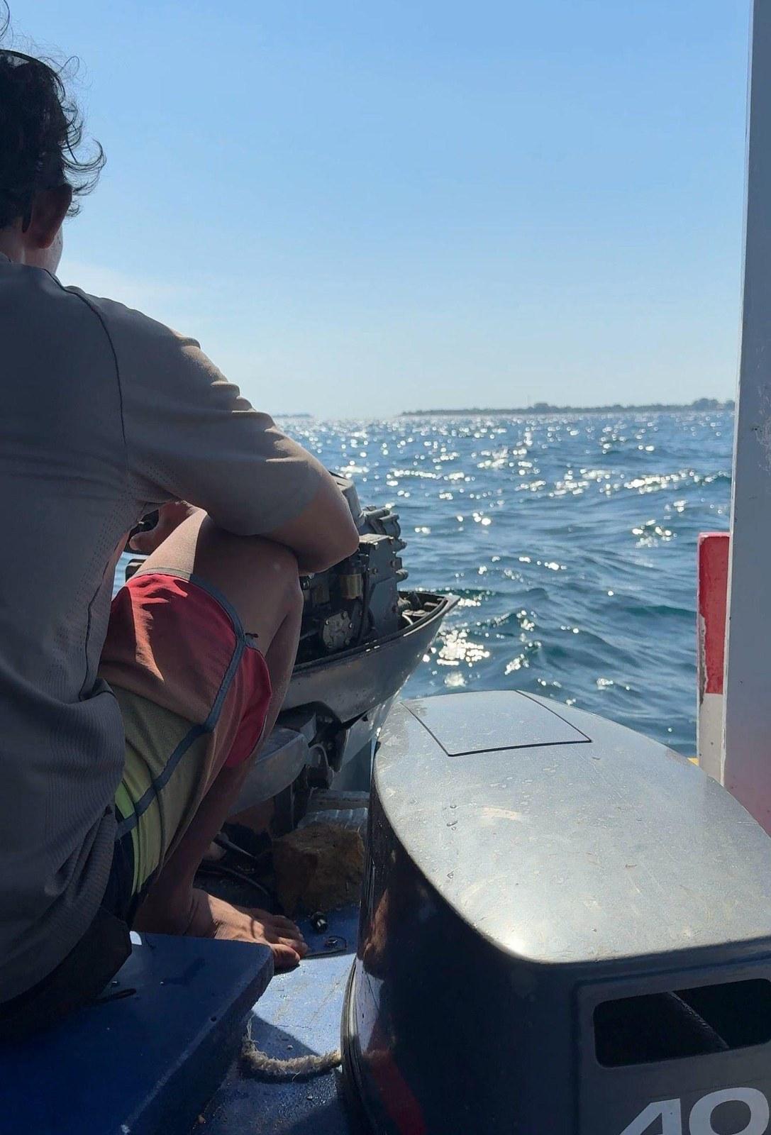 A crew member beside the outboard engine of a small boat in open water
