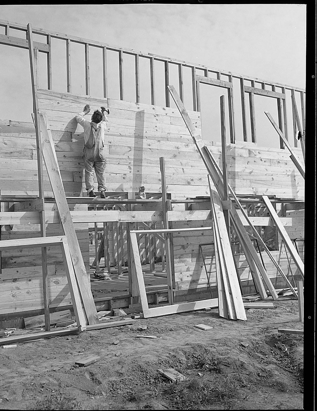 A carpenter nailing boards to a light timber frame on a housing site in 1941