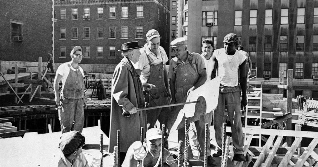 Frank Lloyd Wright in a hat and overcoat with construction workers on the Guggenheim site