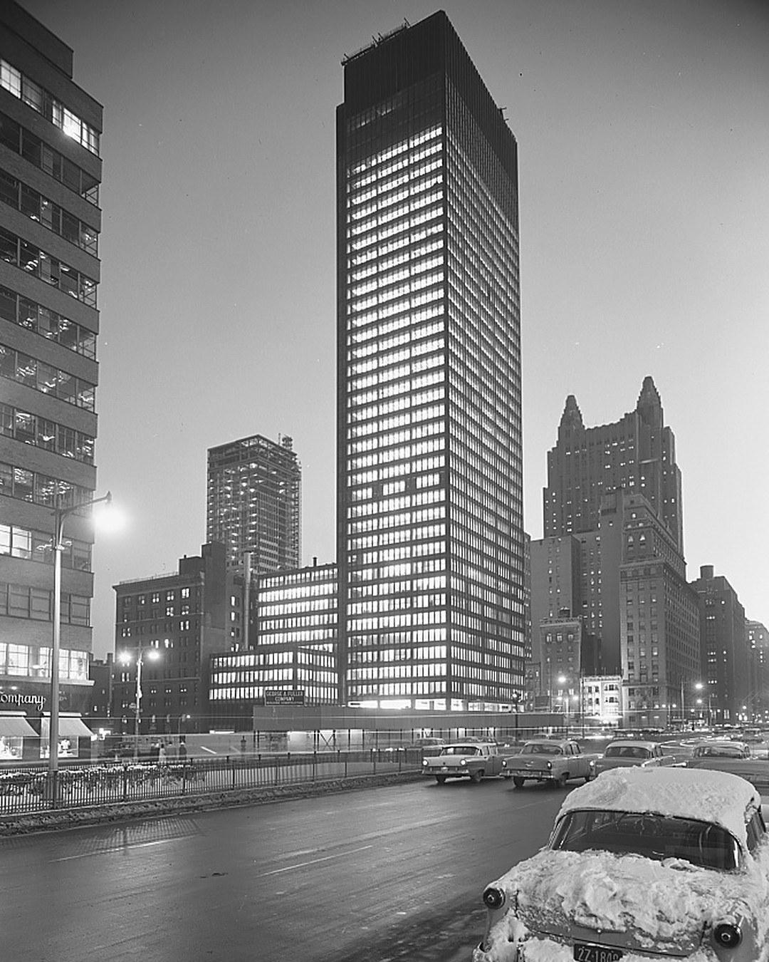 The Seagram Building lit up at night in 1958, snow on the cars in the street