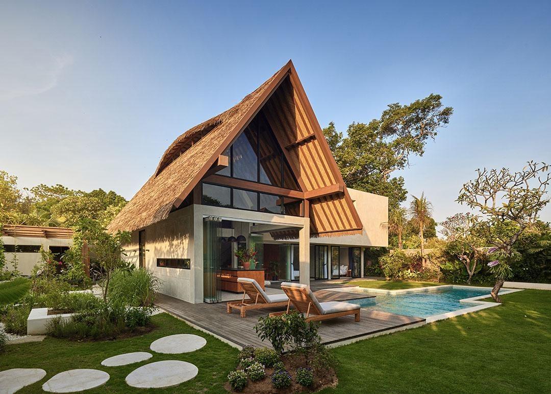 A tropical modern villa with a steep thatched roof, glass gable, deck and pool