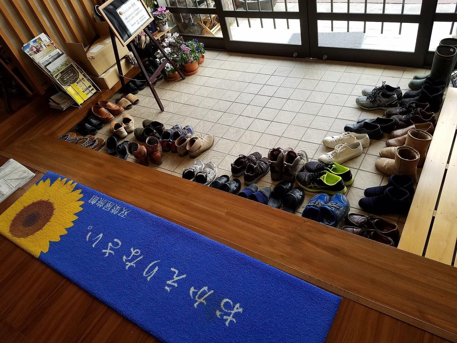 A Japanese genkan: rows of shoes on the sunken tiled entry below a wooden step and a welcome mat